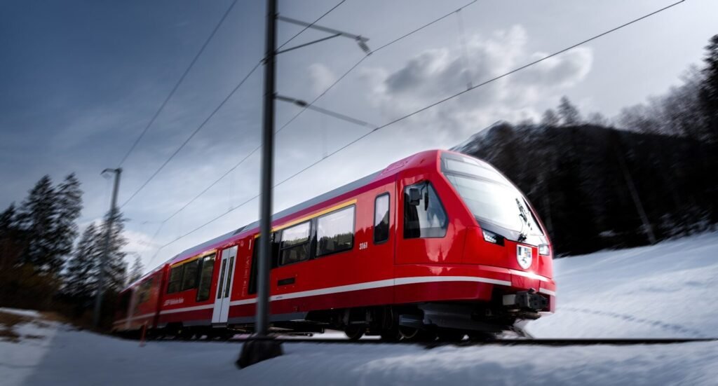 Red train on tracks in a snowy mountain landscape